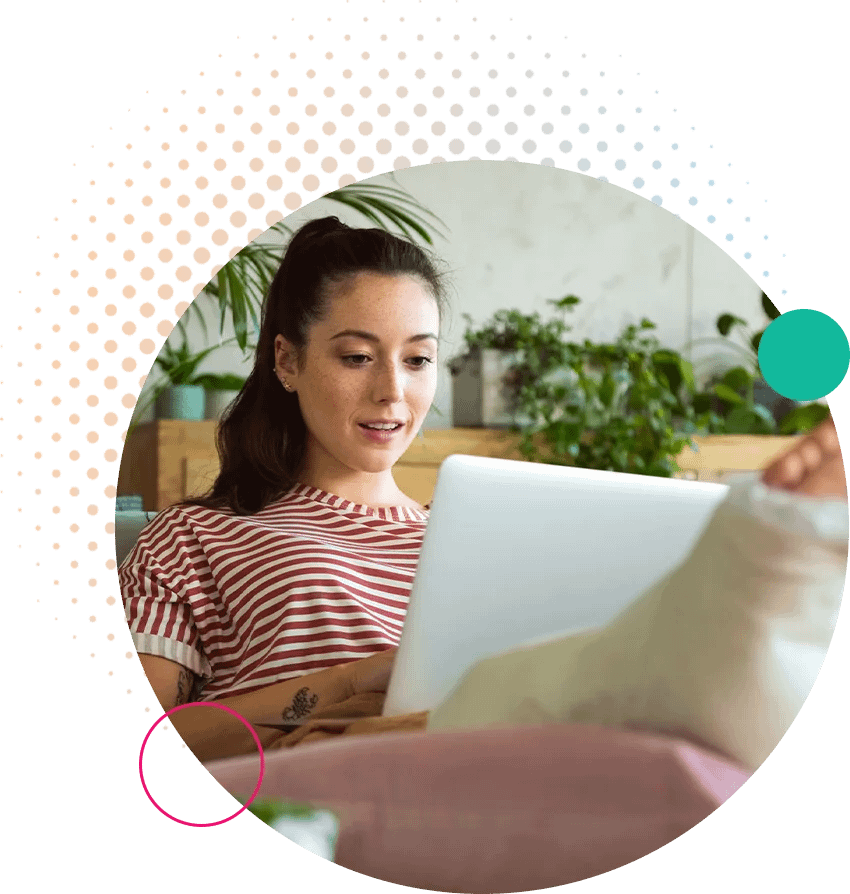 A woman sitting comfortably with her leg in a cast, working on a laptop placed on a table in front of her, suggesting resilience and adaptability in overcoming physical challenges.
